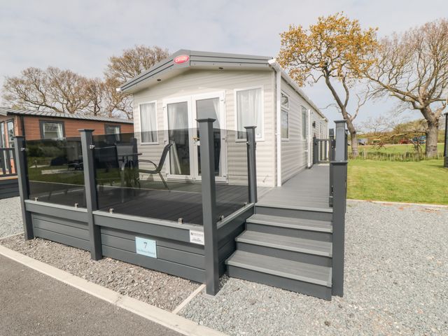 A mobile home with a glass railing deck and stairs on a gravel and grass lot at Lodge 7 - Seabreeze Retreat in Bridlington