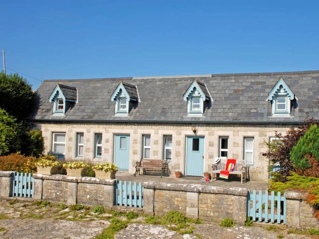 A stone cottage with blue doors and dormer windows with planters on the wall and benches outside at The Hen House Southerndown near St Brides Major