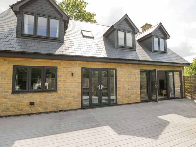 The exterior of a house with yellow brick walls grey roof and multiple black framed windows and doors opening onto a wooden deck at Greystones in Upton St Leonards