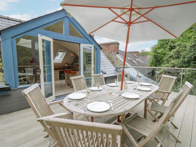 An outdoor dining area with wooden table and chairs under a large umbrella on a balcony at Tan y Craig in Solva
