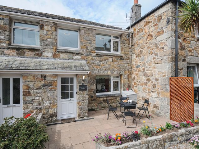 A stone cottage exterior with a small patio table and chairs and a flower bed at Wheal Charlotte Cottage in Perranuthnoe near Goldsithney
