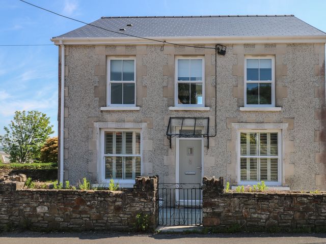 A two story house with four windows a front door and a stone wall with a gate at Gwynfryn in Pen-Clawdd