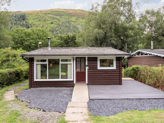A small wooden cabin with a pathway leading to the door surrounded by trees and hills at Chalet 2 in Dinas Mawddwy