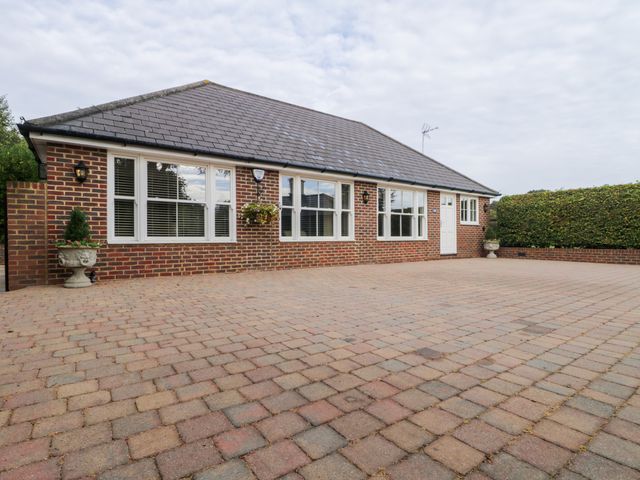 A brick house with multiple windows and a white door on a paved driveway with potted plants and a hedge in the background at Little Aluph in Wye