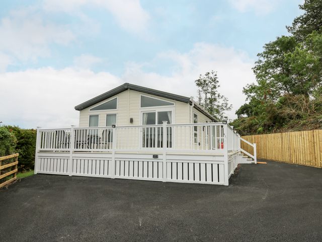 A single story house with white railing and gate with paved driveway and trees at Platinum Lodge in Borth