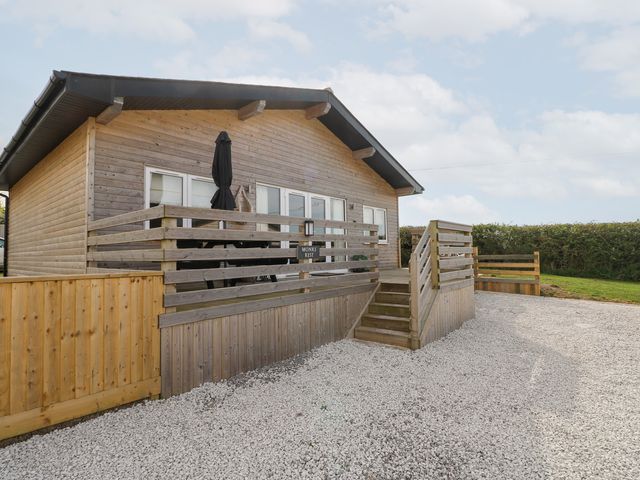 A wooden cabin with a fenced porch and stairs leading to a gravel driveway at Monks Rest in Monknash