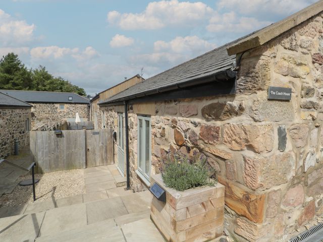 Stone building exterior with wooden planter and fenced patio area at The Coach House in Bamburgh