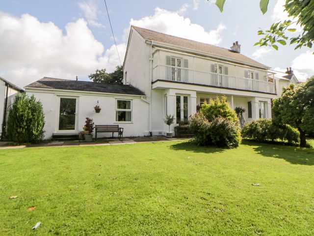 A white two-story house with a balcony and a garden with bushes and grass at Little Claremont in Dousland near Yelverton