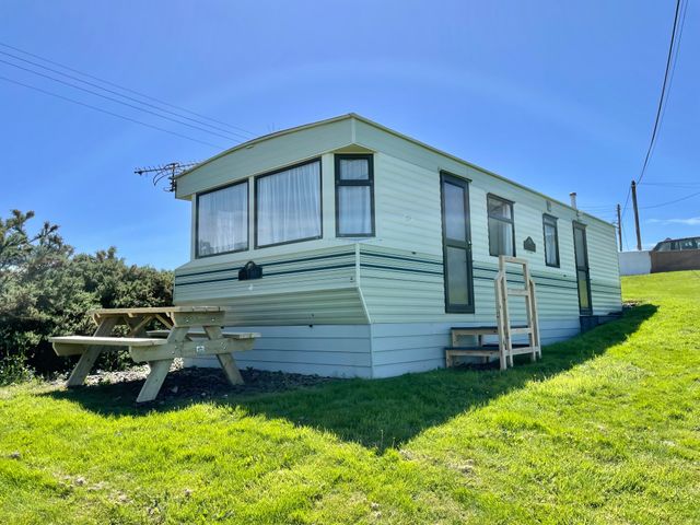 A caravan on grass with a wooden picnic table outside at Caravan at Cartref in Bwlchtocyn near Abersoch