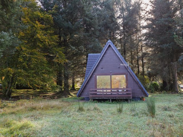 A wooden A-frame cabin with a small porch surrounded by trees at 27 Invergarry Lodges in South Laggan near Invergarry
