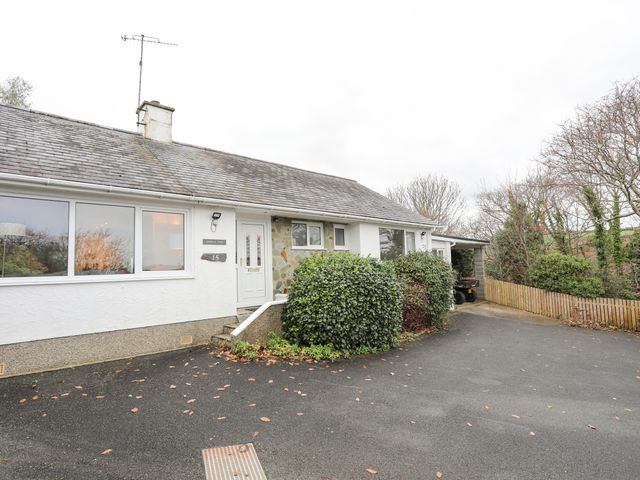 The exterior of a single-story house with a white front door bushes in front and a paved driveway at 15 Maes Awel in Abersoch