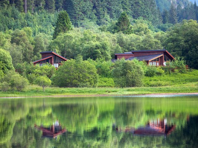Two wooden houses surrounded by trees reflected in a lake at Strathyre Classic Golden Oak Lochside Strathyre Ben Ledi
