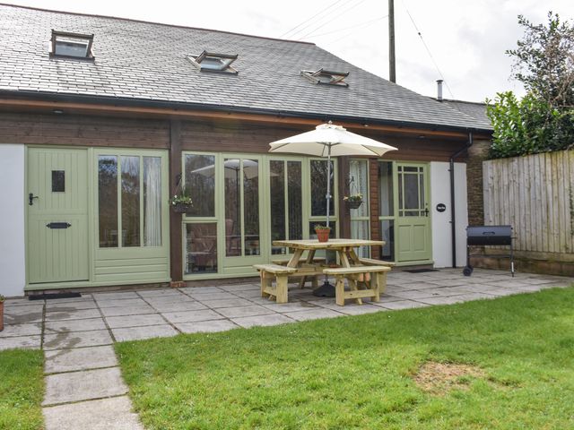 A patio area with a wooden picnic table and umbrella outside a building with green doors and windows at Valley View in Muddiford near West Down