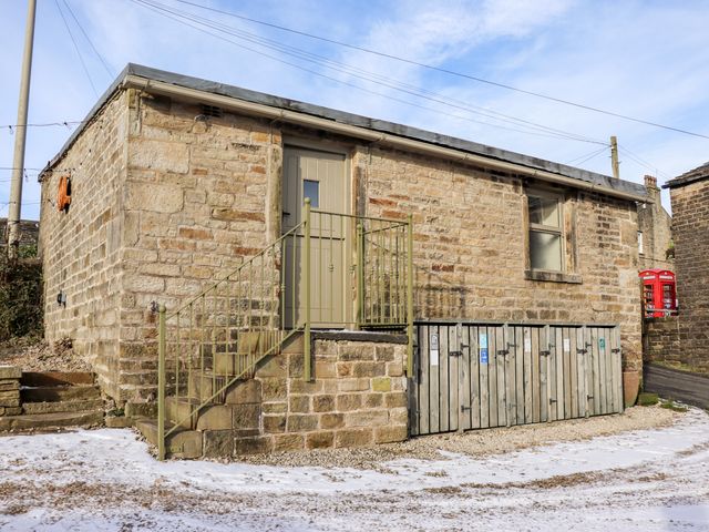 A stone building with a door accessed by stairs and wooden storage lockers at the base in a snowy area at The Shearer's Hut in Holme West Yorkshire