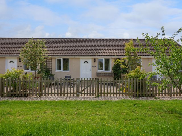 A single-story beige house with a tiled roof white doors front gardens and a wooden picket fence at Widgeon Watchfield in Highbridge
