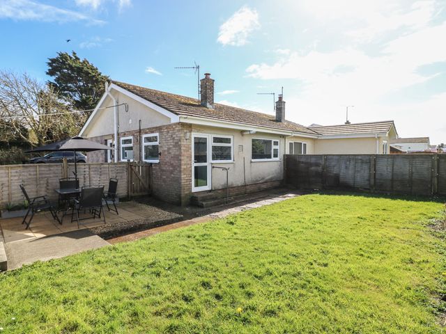 A backyard with a grass lawn and a patio area with outdoor furniture and an umbrella at Plas Nev in St Davids