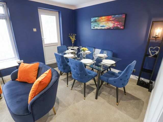 A dining room with blue chairs around a glass table and a blue sofa with orange cushions at Shirleys in Stratford-Upon-Avon