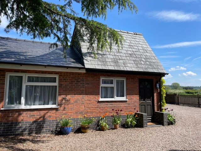 The exterior of a brick house with two windows a black door flower pots on a gravel driveway at Harvest Moon Cottage in Much Cowarne
