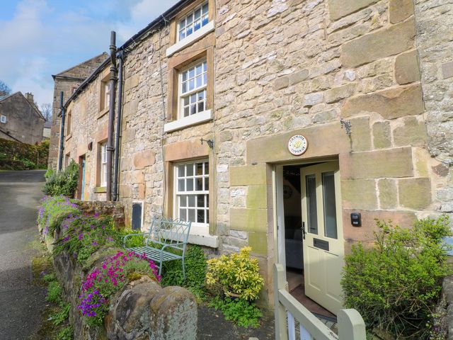Stone cottage exterior with open door bench and flowers at Jasmine Cottage in Winster