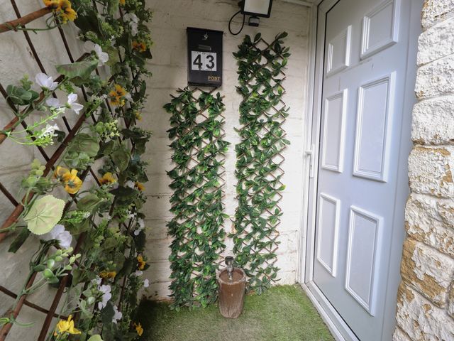 An entrance area with a white door a black mailbox with the number 43 two wooden trellises with green leaves and a small plant pot on grass at Basement Flat 43 in Haworth
