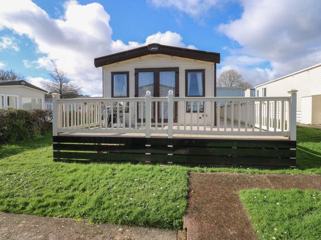 A mobile home with a wooden deck and white railing on a grassy plot at A La Mer in Paignton
