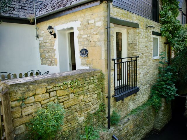 Exterior view of a stone cottage with a small balcony black railing and greenery at Windrush in Burford