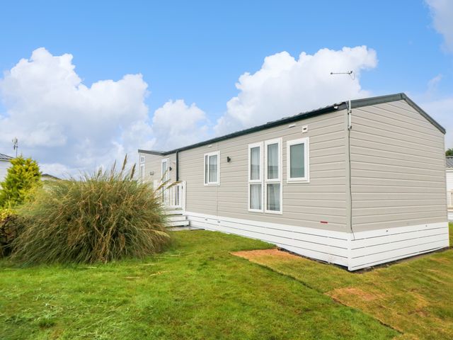 A beige mobile home with white trim on grass under a blue sky at Finch 65 in Cayton Bay