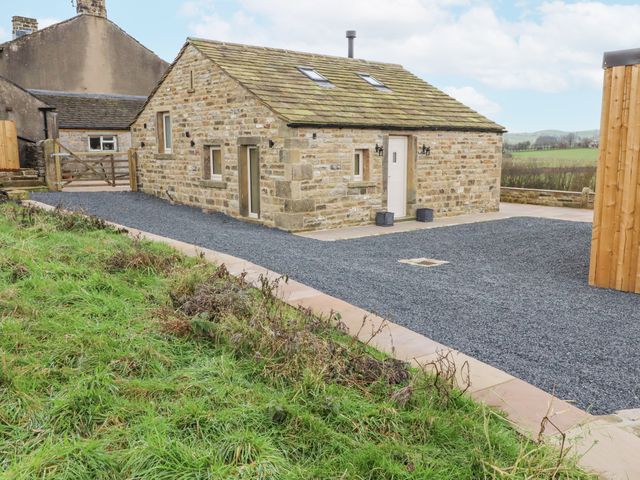 A stone cottage with a gravel driveway and green field in the background at Croft Cottage in Gargrave