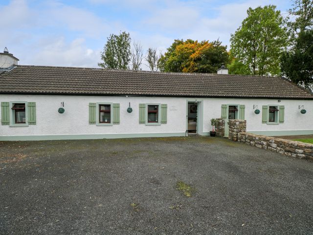 A single story house with green window shutters and an open door surrounded by trees at Gort Farm Cottage Jamestown near Drumsna