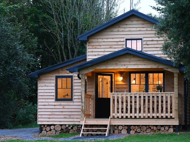 A wooden cabin with a porch and stacked firewood under at Walden Lodge in Tresillian Wood near Llantwit Major
