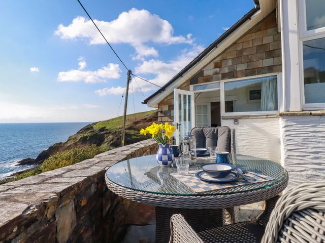 An outdoor stone terrace with a round glass table set for a meal overlooking a coastal view at Suntrap House in Portloe