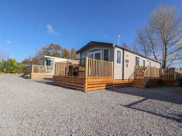 Two static caravans with wooden decks on a gravel lot with trees in the background at Carmina in Warton Lancashire