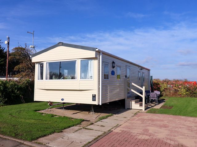 A beige mobile home with steps and outdoor chairs on grass at No 58 Westfield in Skipsea
