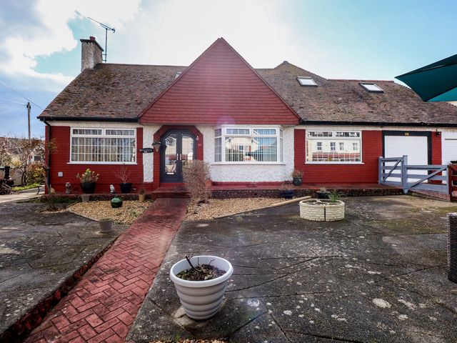 A red and white house with a sloped roof and black front door with a paved path and planters outside at Bryn-Y-Glyn in Penrhyn Bay