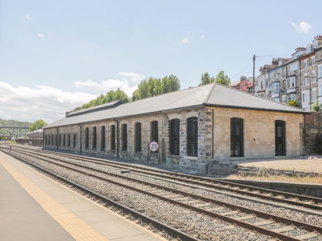 A railway platform with train tracks and a long stone building with multiple windows at Duchess of Hamilton @ Engine Shed in Whitby