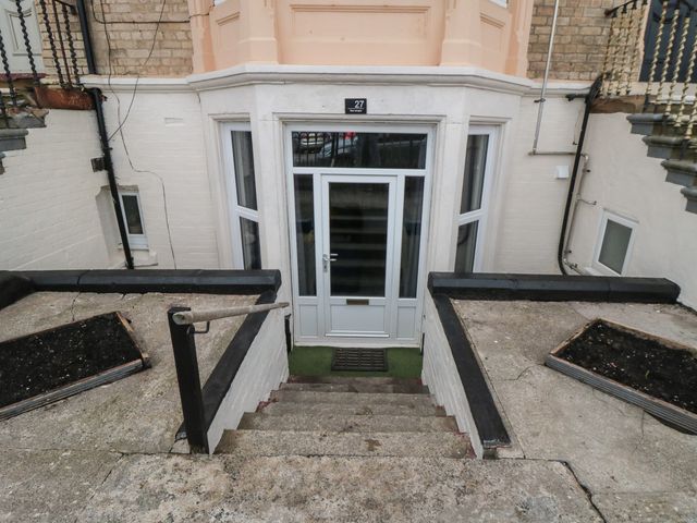 Stairs leading down to a white door with glass panels between two raised concrete areas with planter boxes at The Sea Escape in Saltburn-By-The-Sea