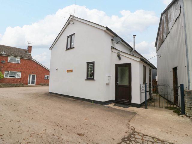 A white detached house with dark framed windows and door next to a metal building at The Old Dairy in Allensmore