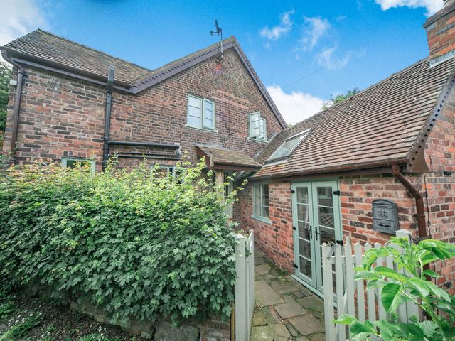 An exterior view of a brick house with green framed windows and doors surrounded by a white picket fence and greenery at Sleepy Hollow in Jackfield near Ironbridge Gorge