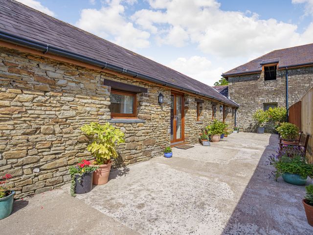An outdoor stone courtyard with potted plants and benches at The Dairy in Penuel near Llanmorlais