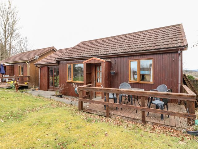 A wooden house with a small deck and plastic chairs in a grassy yard at Glen Pean in Corpach near Fort William