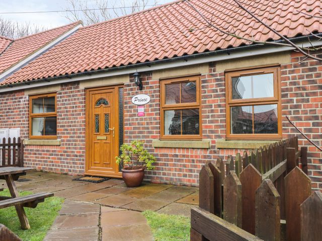 A brick cottage with wooden door and windows a potted plant on the patio and wooden fence at Prince Cottage in Skinningrove near Whitby