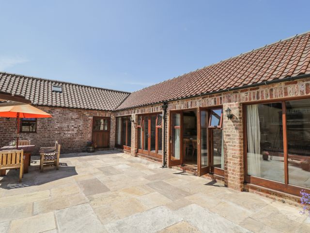 An outdoor patio area with stone paving wooden table and chairs and umbrella at Wheelhouse Cottage in Sowerby outskirts of Thirsk
