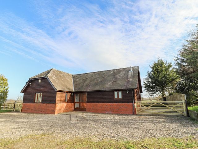 A detached house with wooden and brick exterior surrounded by trees and a gravel driveway at Hill Farm Cottage in Kerrys Gate near Abbey Dore