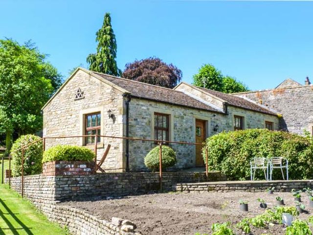 A stone house with windows and wooden doors surrounded by greenery and a garden at The Summer Palace in Middleham Wensleydale