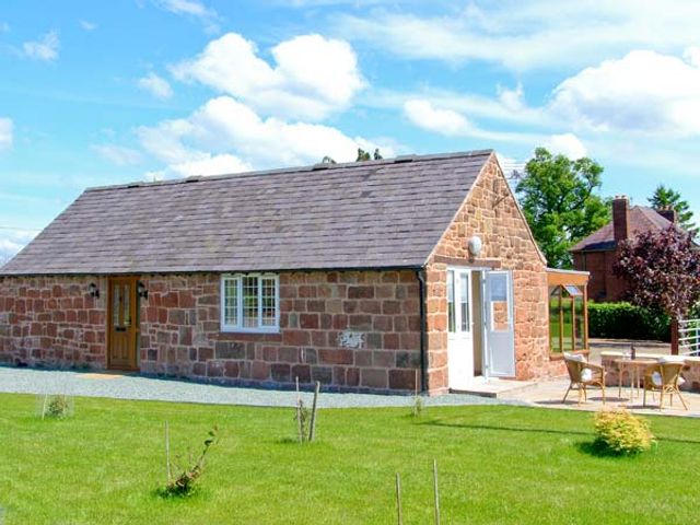 A small stone cottage with a tiled roof and wooden door next to a patio with chairs and a table at Byre Cottage Nesscliffe near Shrewsbury