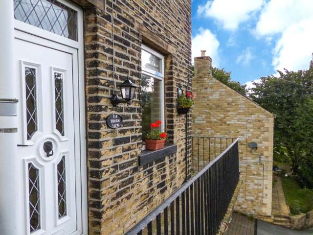 A brick exterior wall with a white door window flowerpots and a black railing at Cottage in the Sky in Luddenden near Hebden Bridge