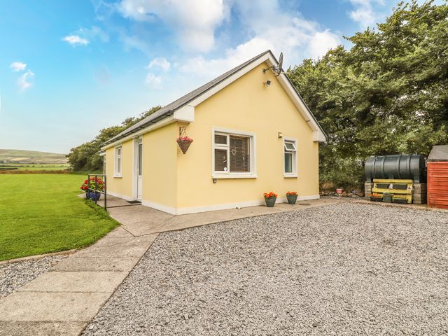 A yellow single-story house with a gravel driveway and green lawn surrounded by trees at Moybella Lodge in Lisselton near Ballybunion County Kerry