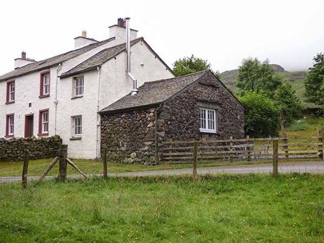 A stone and white cottage with fenced garden and trees in the background at Cockley Beck Cottage Cockley Beck near Broughton-in-Furness
