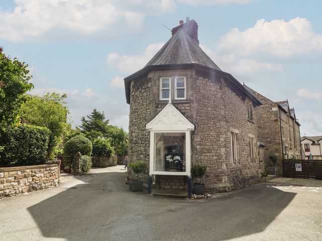 A stone building with a pointed roof and a white bay window on a street corner at Lonsdale Cottage in Kirkby Lonsdale