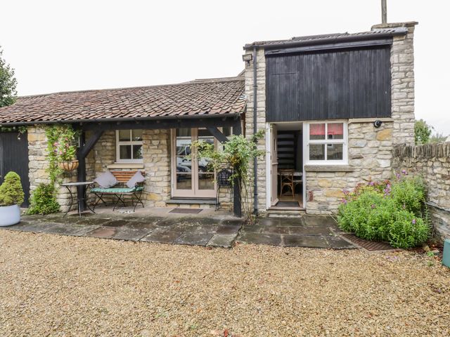 Stone cottage exterior with gravel driveway wooden bench and table outside at The Coach House in Bitton